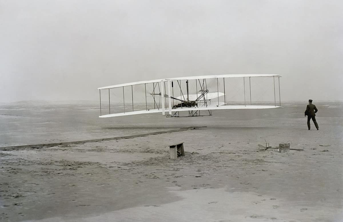 The Wright Flyer leaving the ground at Kitty Hawk in 1903 with Wilbur Wright running alongside